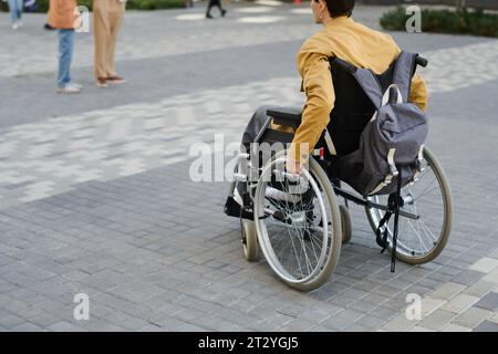 Rear view of young man with disability using wheelchair to move along the street Stock Photo