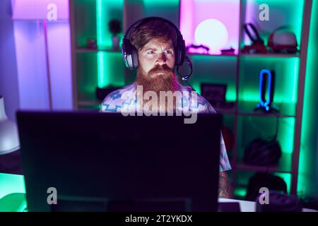 Young redhead man streamer playing video game using computer at gaming room Stock Photo