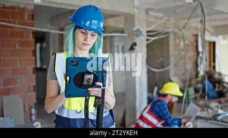 Man and woman builders using touchpad reading house project at construction site Stock Photo