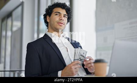 Young latin man business worker using laptop counting dollars at office Stock Photo