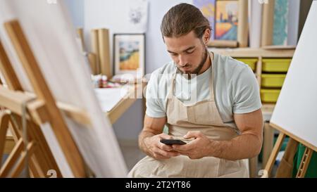 Young hispanic man artist using smartphone at art studio Stock Photo