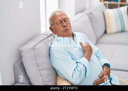 Senior grey-haired man suffering for heart attack sitting on sofa at home Stock Photo