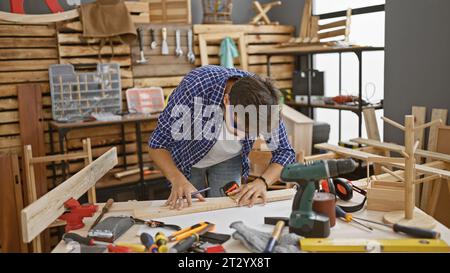 Handsome young arab man, a professional carpenter, concentrated on drawing a mark on a wood plank, fully engrossed in his carpentry work inside the wo Stock Photo