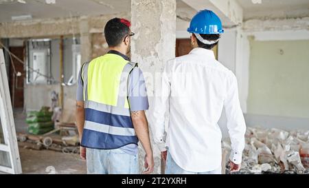 Two men builder and architect standing together backwards at construction site Stock Photo
