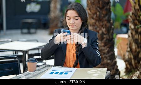 Young beautiful hispanic woman business worker making photo to documents at coffee shop terrace Stock Photo