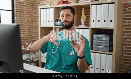Young hispanic man doctor holding doughnut doing thumb down gesture at the clinic Stock Photo
