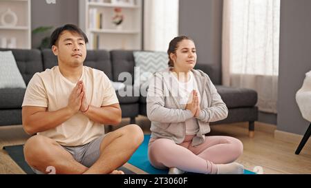 Man and woman couple sitting on floor doing yoga exercise at home Stock Photo