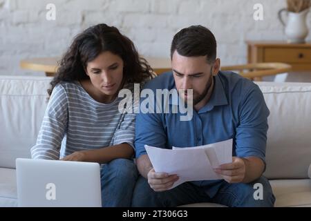 Focused married couple reading paper documents at laptop Stock Photo