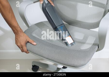 The man is using a cordless car vacuum cleaner to clean the gray chairs in the office. Stock Photo