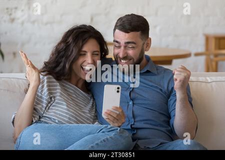 Happy excited adult dating couple using smartphone, staring at screen Stock Photo