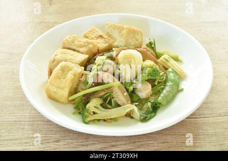 stir fried slice cabbage broccoli with green pea and straw mushroom couple dice tofu in soy sauce vegetarian food on plate Stock Photo