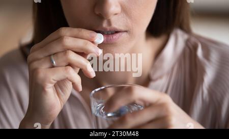 Close up view woman holding glass of water takes pill Stock Photo