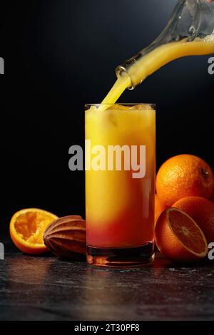 https://l450v.alamy.com/450v/2t30pf8/cocktail-tequila-sunrise-with-ice-and-grenadine-on-a-black-background-orange-juice-is-poured-from-a-bottle-into-a-glass-with-ice-and-syrup-2t30pf8.jpg