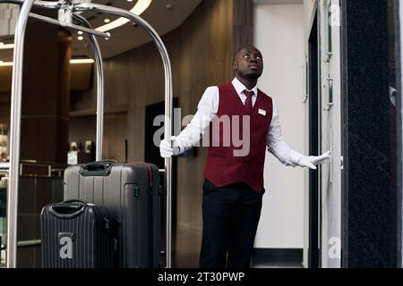 African American doorman with trolley with luggage waiting for the elevator in the hall of hotel Stock Photo
