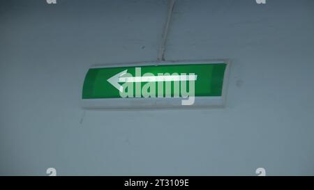 Glowing green arrow on wall. Clip. Arrow on green background lights up to indicate exit. Arrow of evacuation exit glows with green background on wall Stock Photo