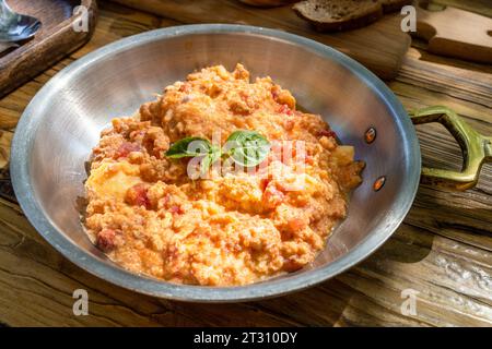 frying pan with omelette with tomatoes, decorated with fresh green basil leaves on wooden table in street cafe on sunny morning Stock Photo