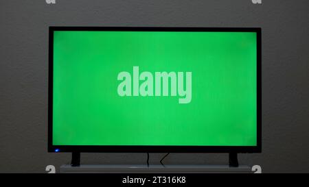 LcD smart TV with green screen on a grey wall background in the living room. Concept. Chroma key screen of a modern TV. Stock Photo