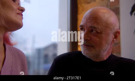 An elderly couple is sitting in a cafe at a table and communicating. Stock footage. Woman and a man aged on a date in a restaurant celebrating. Stock Photo