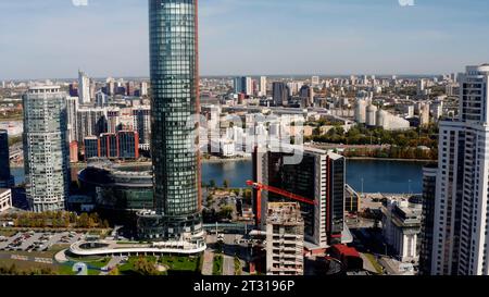 Summer cityscape and a wide river flowing along the buildings. Stock footage. Construction site and working crane in the city. Stock Photo