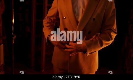 A man in a brown jacket fastens the buttons in a dark room. Stock footage. Flashing lights indoors. Stock Photo