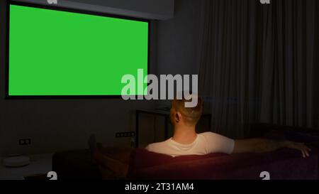 Viewing on a projector in a closed room. Media. A man looking into a green screen that is shown on a large screen. Stock Photo