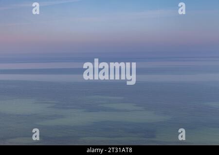 Blue sky with haze and blurry glowing pink clouds above the sea. Shallow coastal sea water with azure patterns. Ripples in the water Stock Photo