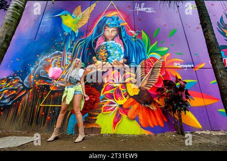 Medellin, Colombia - January 9, 2023: Young tourist woman poses for a photograph next to a mural painting in the streets of Comuna 13 Stock Photo