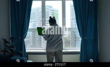 Green screen on the computer. Media. A woman and a man holding a small laptop with a green screen in front of the window in the room. Stock Photo