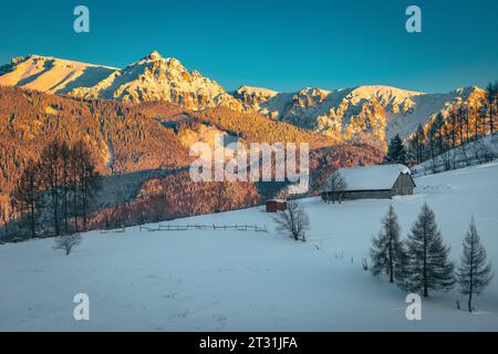 Beautiful winter landscape with snow covered wooden hut on the slope and majestic high mountains in background at sunset, Bucegi mountains, Carpathian Stock Photo
