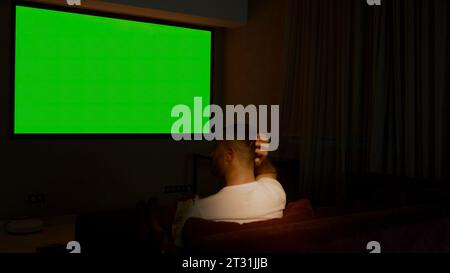 Viewing on a projector in a closed room. Media. A man looking into a green screen that is shown on a large screen. Stock Photo
