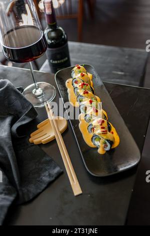 Sushi roll with tuna and vegetables in sauce on a black plate in a restaurant. High quality photo Stock Photo