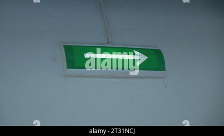 Glowing green arrow on wall. Clip. Arrow on green background lights up to indicate exit. Arrow of evacuation exit glows with green background on wall Stock Photo