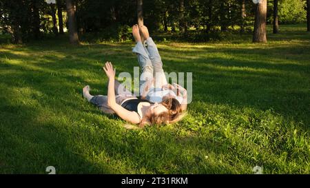 Friends are lying on green grass in park on sunny summer day. Concept. Beautiful girlfriends are lying on green grass in park. Relaxing in park on Stock Photo
