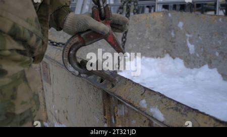Close-up of builder hooking hook to load. Clip. Fixing hook to lift load. Hook trailer to heavy load for lifting by crane Stock Photo