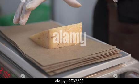 Weighs piece of cheese. Art. Weighing cheese for sale. Seller weighs piece of cheese for sale. Cheese factory and shops Stock Photo