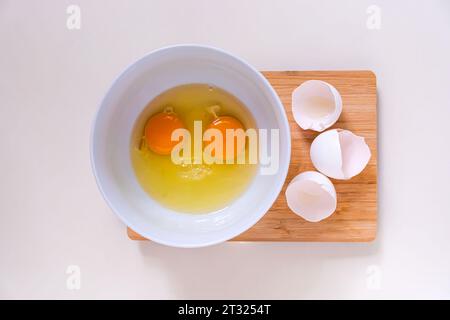 Bright yellow egg yolks in a white bowl and eggshells on a bamboo cutting board. Stock Photo