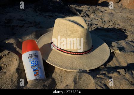 Sun cream bottle and a Panama sun hat in the sand on a beach on Ilha do Farol (Lighthouse Island) off the coast of Olhão in Portugal. Stock Photo