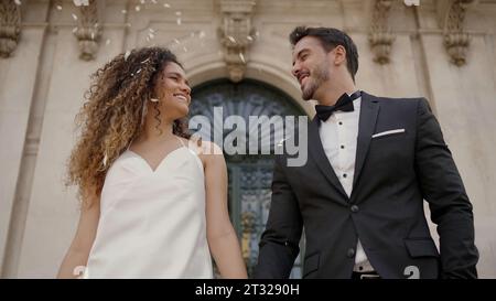 Bride and groom walking down while guests toss petals at wedding. Action. Wife and husband by the church. Stock Photo