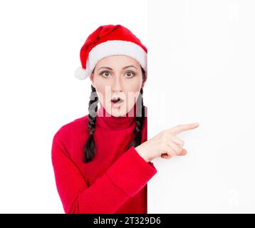 Surprised Woman in Santa Hat pointing with her finger on banner isolated on a white background. Sale concept. Stock Photo