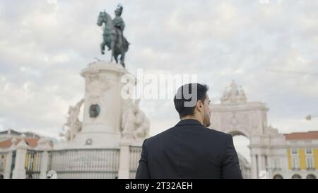 Rear view of joyful middle aged businessman in suit walking outdoors in city square. Action. People and urban background concept. Stock Photo