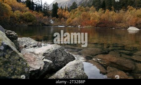 Wide beautiful lake with green and yellow trees and big stones on the shore. Creative. Amazing clean transparent water. Stock Photo