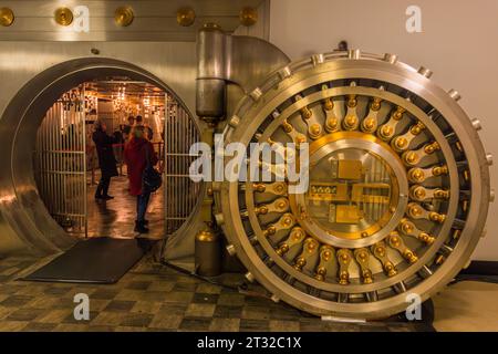 The massive steel vault door of the Central Standard Building in Chicago, Illinois, United States, stands open during the Open House Chicago festival, revealing a barred inner chamber. Two visitors examine the safe-deposit boxes inside. Built in 1924 as a bank hall on LaSalle Street, the building opens its historic vault to the public once a year during the event, organised by the Chicago Architecture Center since 2011. Stock Photo