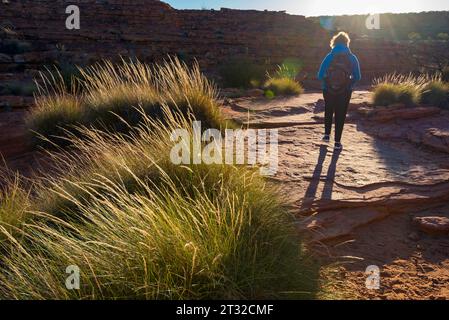 A woman walking into morning sunlight over the rocky landscape on  the Rim Walk at Kings Canyon (Watarrka) in the Northern Territory, Australia Stock Photo