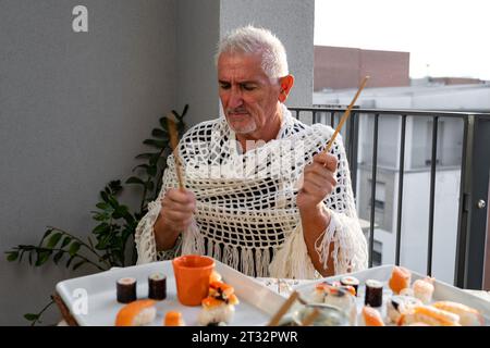 attractive middle-aged man have fun while eating sitting at a table laid Chinese take away food on a terrace outdoors Stock Photo