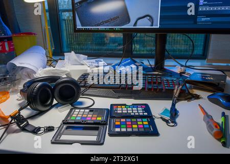 Two X-rite ColorChecker passports laying on the messy desk of a photographer, together with a keyboard, headphones and a monitor.. Stock Photo