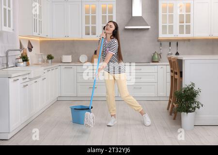 Enjoying cleaning. Woman in headphones listening music and mopping in kitchen Stock Photo