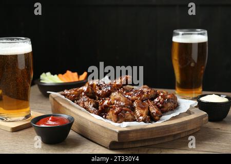 Tasty chicken wings, sauces, vegetable sticks and glasses of beer on wooden table, space for text. Delicious snacks Stock Photo