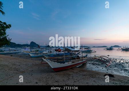 Traditional wooden Filipino banca boats with outriggers anchored on the beach at sunset in tropical paradise Stock Photo