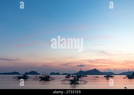 Traditional Filipino banca boats with outriggers anchored offshore at sunset in tropical paradise Stock Photo