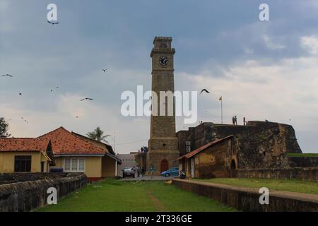 Birds flying over the old clock tower at Galle Dutch Fort 17th Century. Ruined Dutch castle that is UNESCO listed as a World Heritage Site in Sri Lank Stock Photo